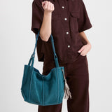 Deep teal suede medium tote bag with dual shoulder straps and tassel charm, worn over shoulder.